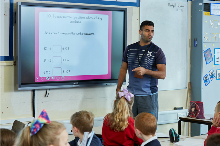 A teacher and a group of school children. The teacher is teaching a Maths lesson.